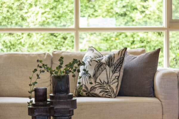 Elegant living room close-up showcasing a plush sofa with cushions and a glass vase inside a bright space.