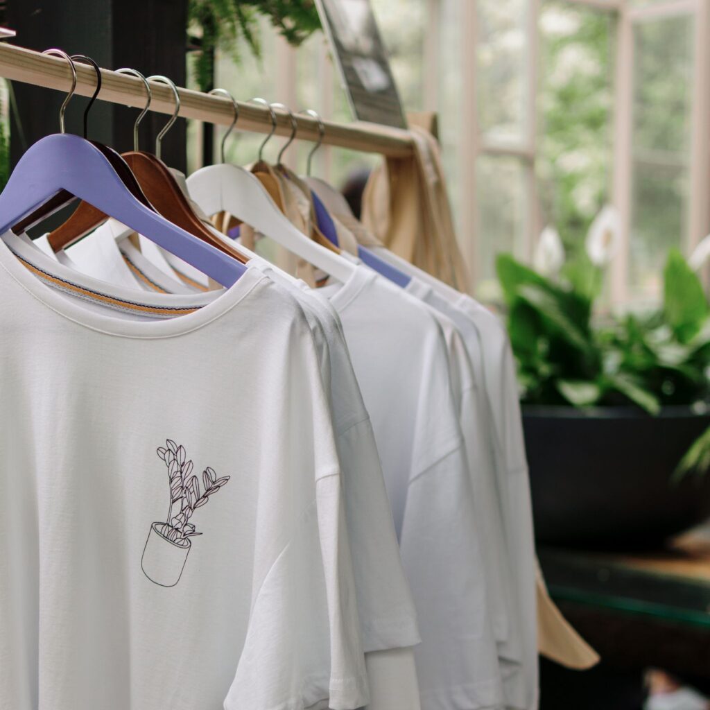 Row of white t-shirts with plant design in a botanical-themed shop interior.