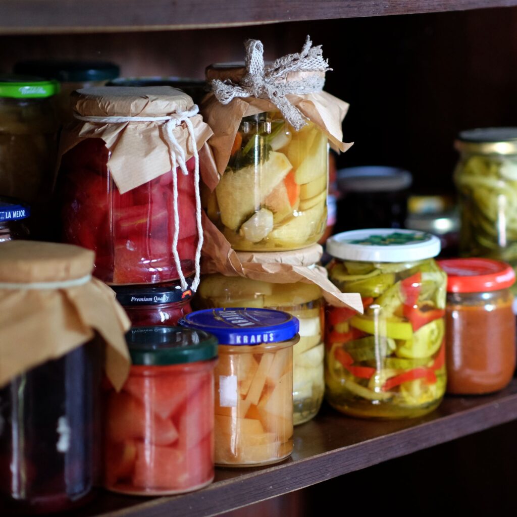 A variety of homemade preserves and pickles stored on a rustic wooden pantry shelf.