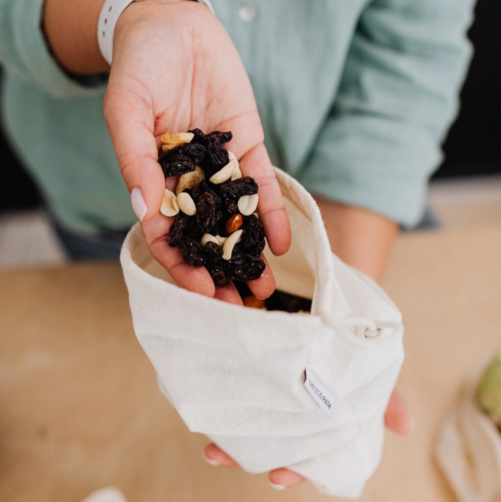 Close-up of a woman's hand holding a mix of raisins and nuts in a fabric bag, promoting healthy snacking.