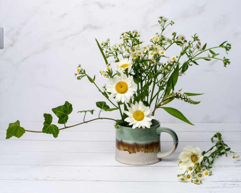 Fresh wildflowers in a ceramic mug on white wooden surface; perfect for natural decor concepts.
