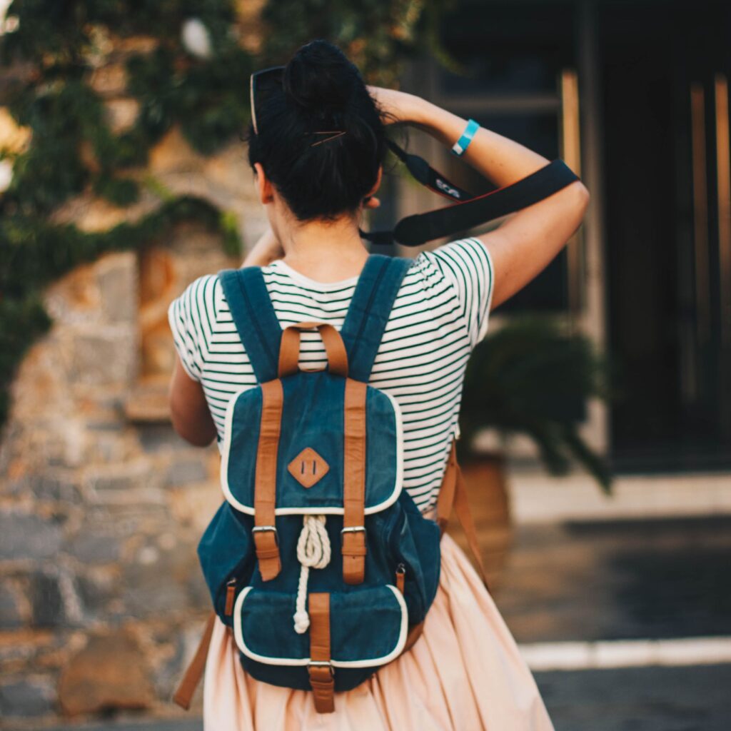 A young woman in casual attire explores a sunny city street with a stylish backpack.