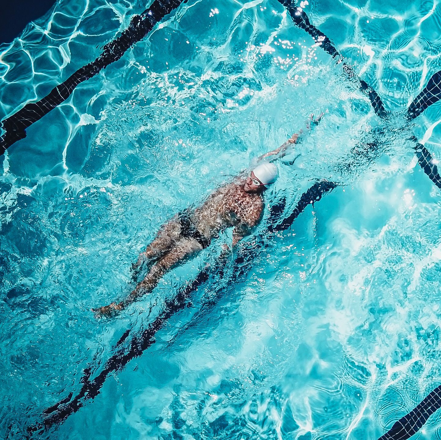 Athlete performing backstroke in a clear turquoise pool viewed from above.
