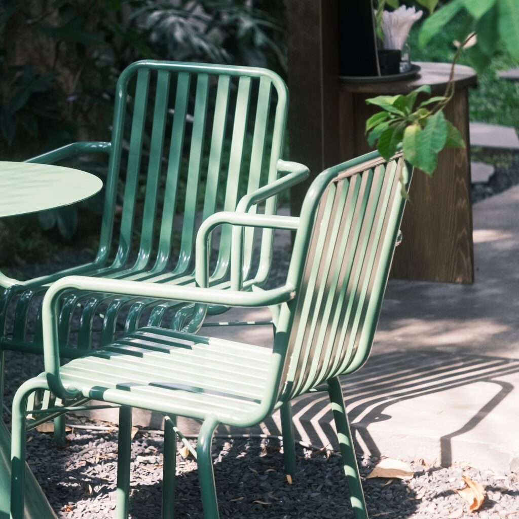 Green metal chairs and table on a sunlit patio surrounded by lush foliage.