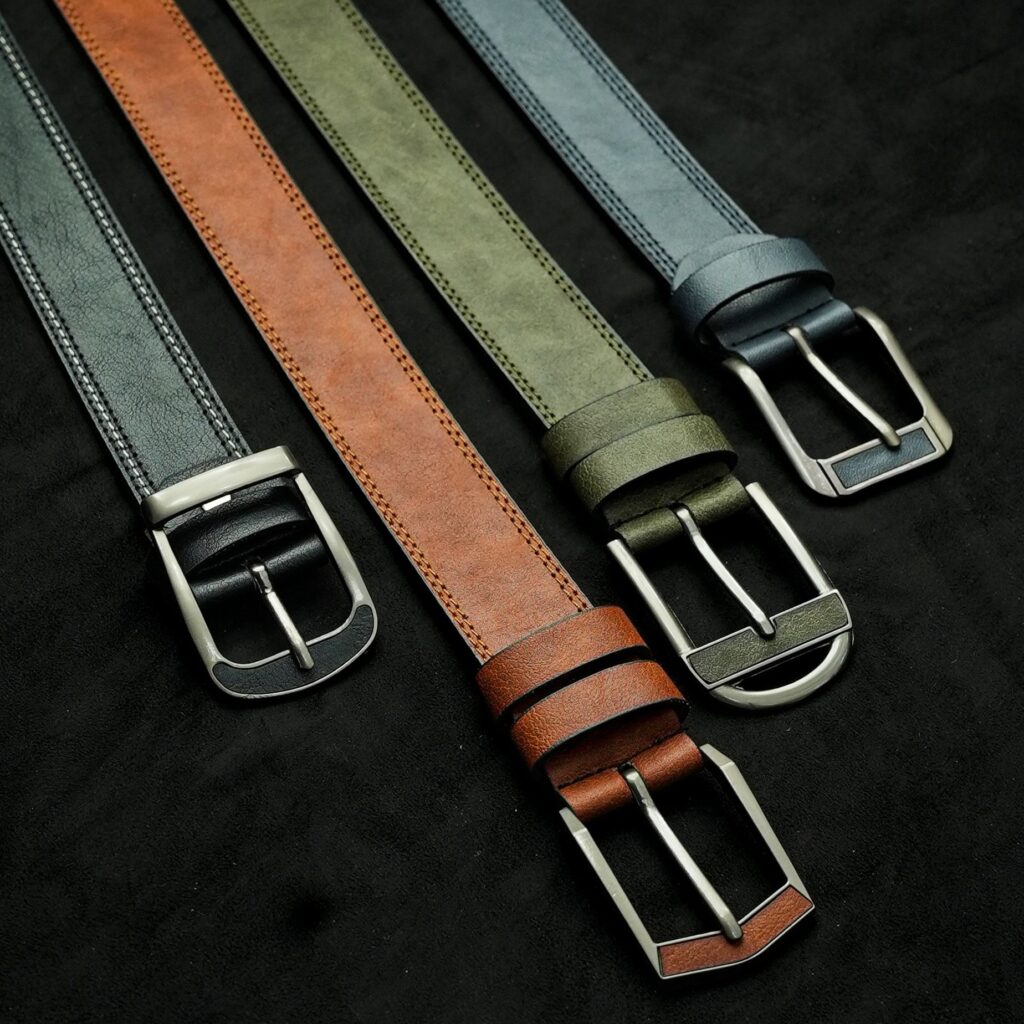 A collection of four stylish leather belts in various colors lying on a black surface.