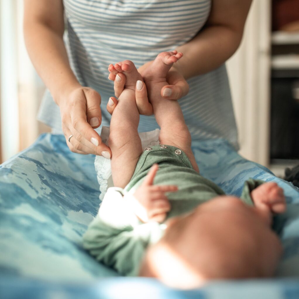 A mother gently changes her baby's diaper indoors with a warm, intimate atmosphere.