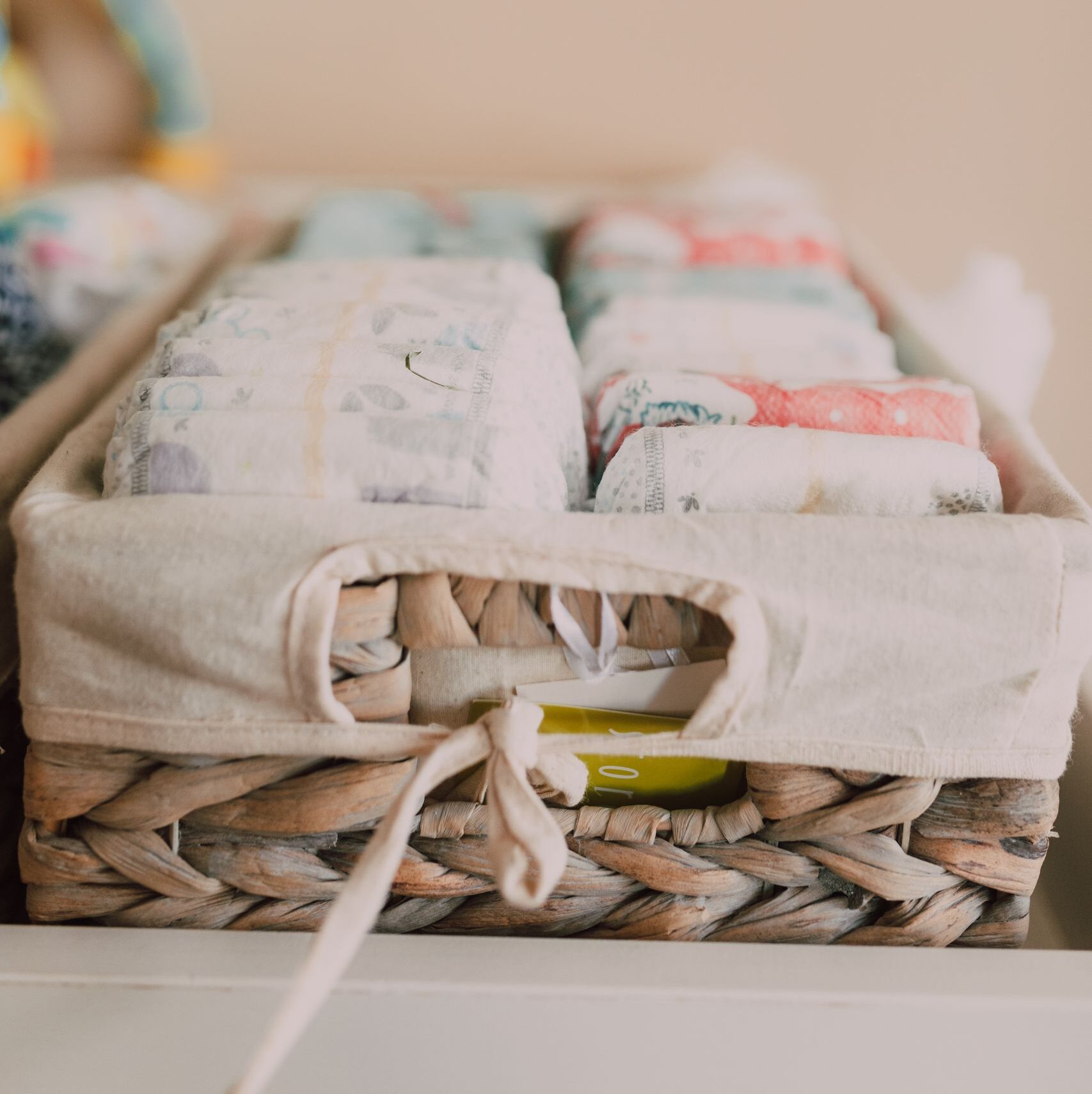 Close-up of a woven basket with neatly arranged baby diapers in a neutral-toned nursery.