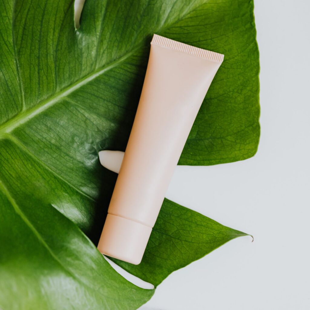 Cream tube on a fresh green leaf against a marble surface, embracing natural beauty themes.