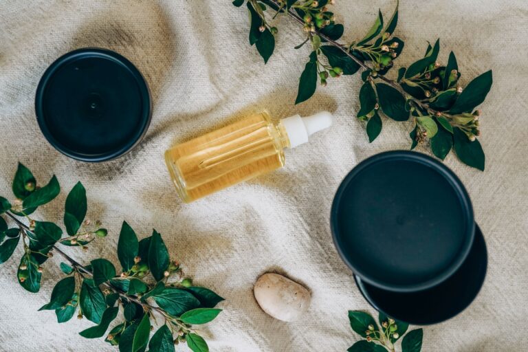 Glass bottle of yellow serum surrounded by green leaves on fabric, showcasing botanical skincare.
