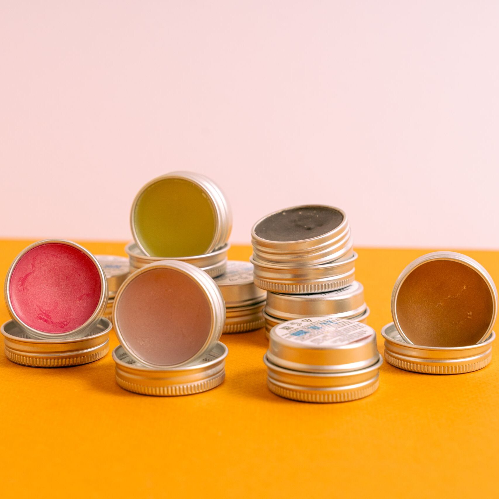 A close-up of assorted lip balms in stackable metal tins on a vibrant background.