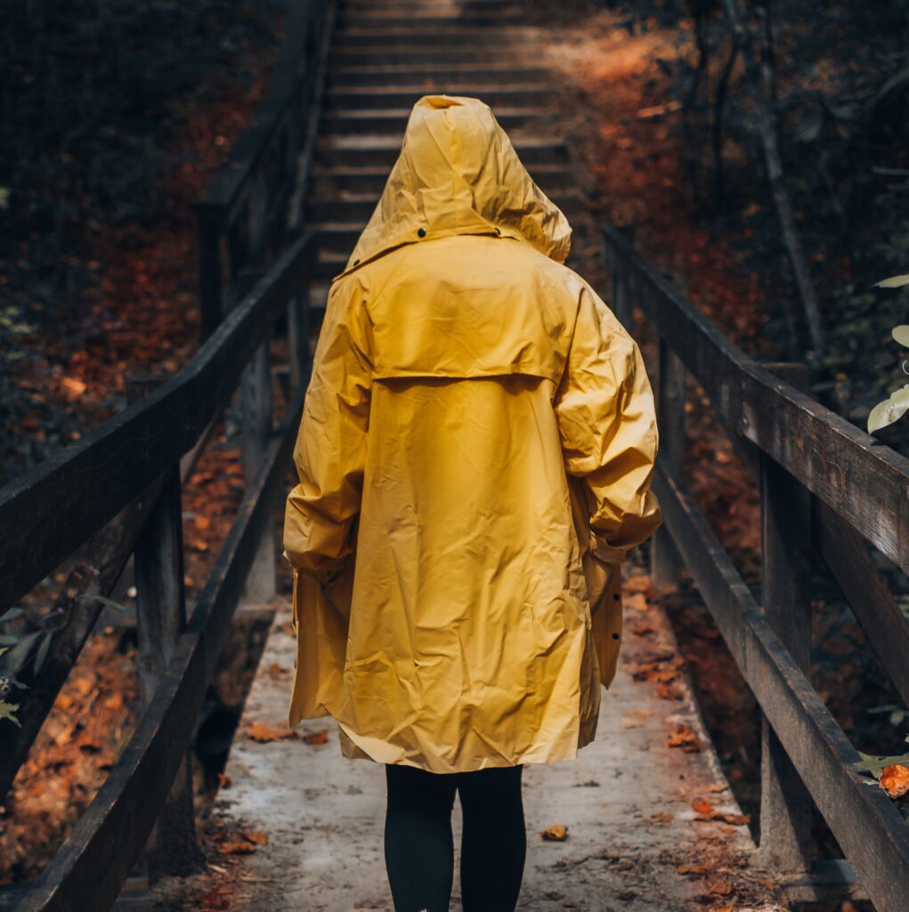 A person in a yellow raincoat walks through a scenic forest on a wooden path during fall.