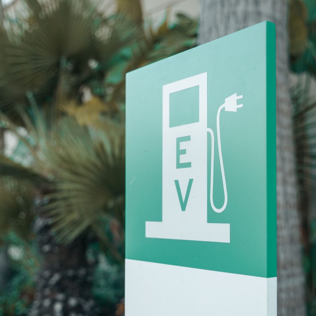 Close-up of a green and white electric vehicle charging station sign with nature background.